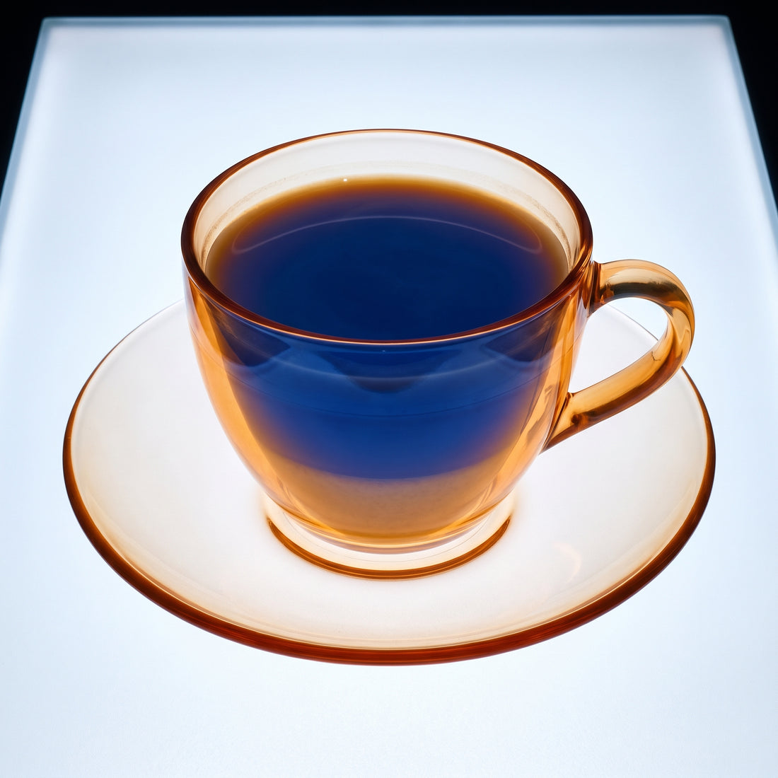 X-ray lightbox image of a flat white coffee cup and saucer, showing amber-orange ceramic outer form and cobalt blue coffee interior