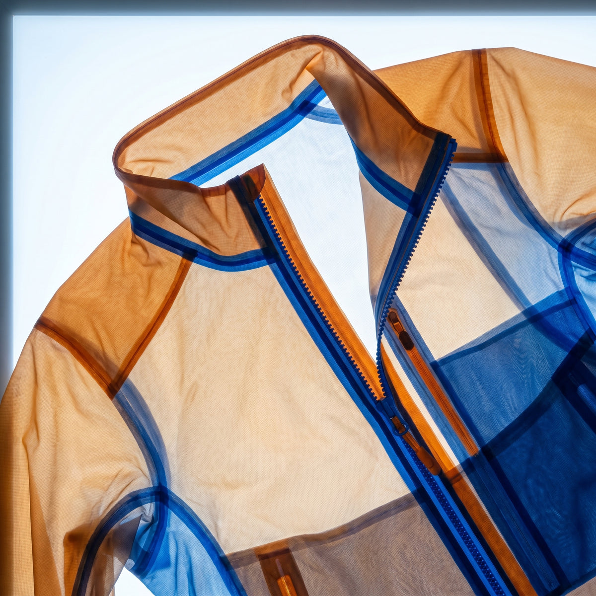 X-ray lightbox image of a technical outerwear jacket collar showing bonded seam construction, amber-orange outer shell with cobalt blue thermoplastic adhesive bond layer visible