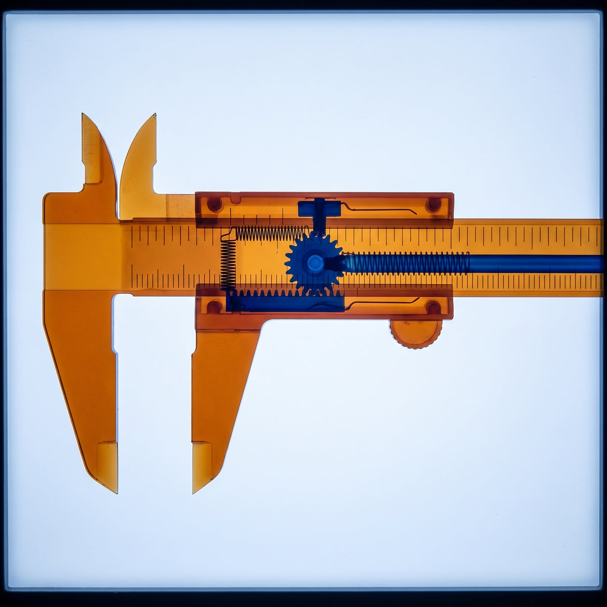 X-ray of precision vernier calipers on an illuminated lightbox, amber-orange outer body with cobalt blue internal measuring mechanism